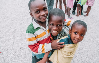 Three Haitian male children hugging and smiling