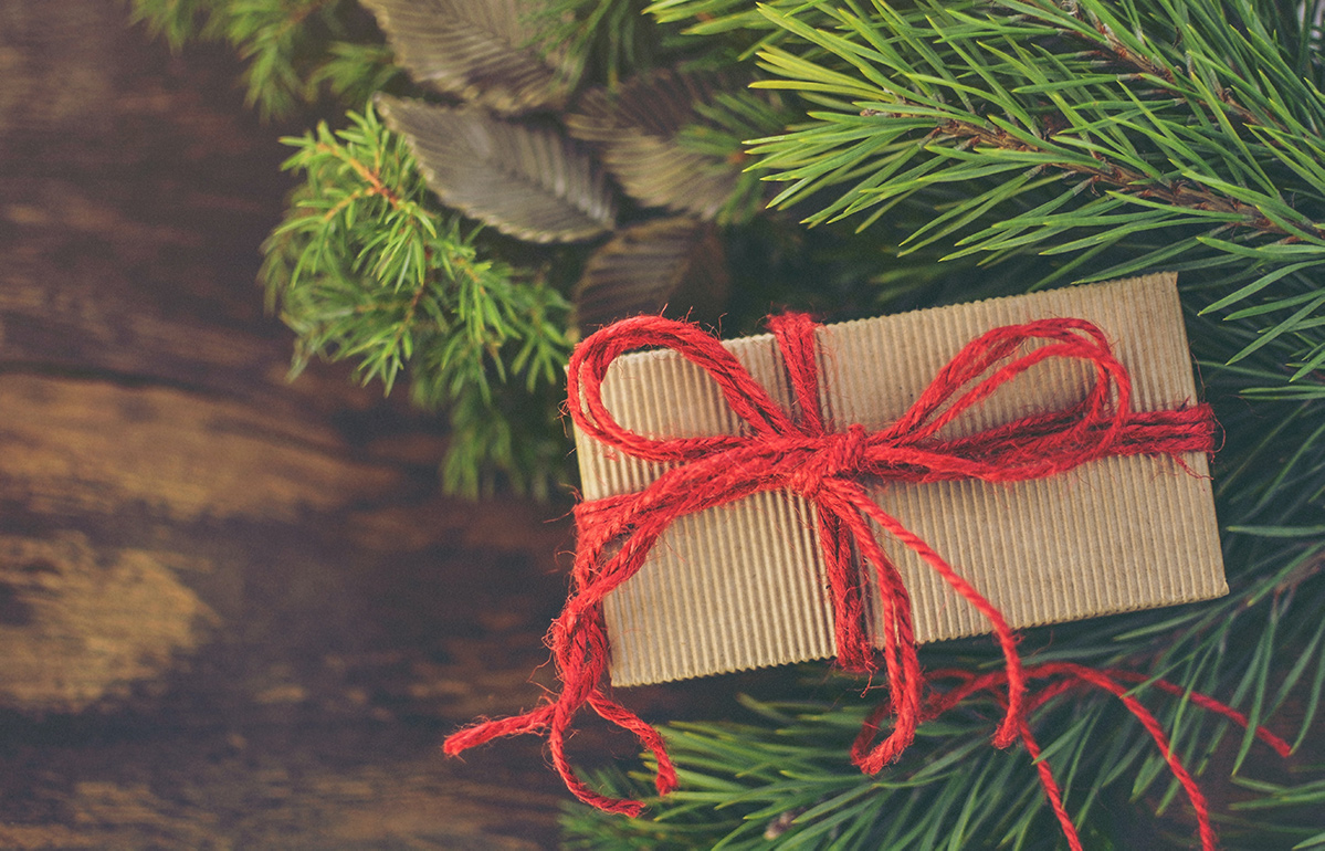 a small box gift wrapped in brown parchment paper with a red yarn bow next to a Christmas wreath.