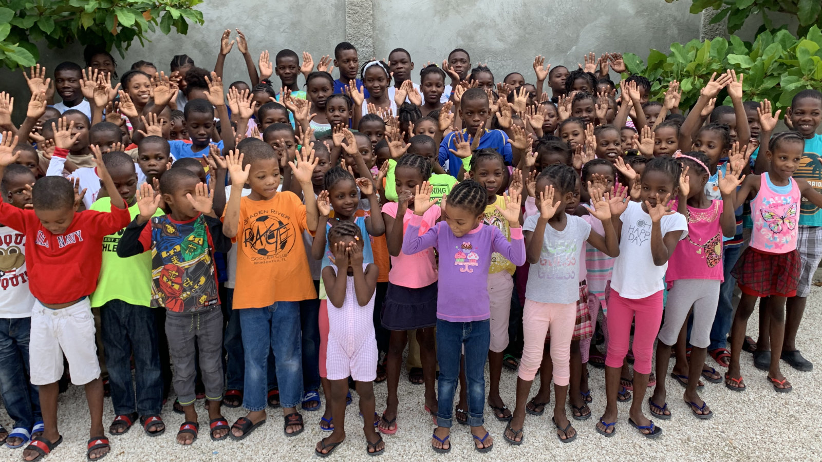 A large group of children with hands up in the air and smiling.