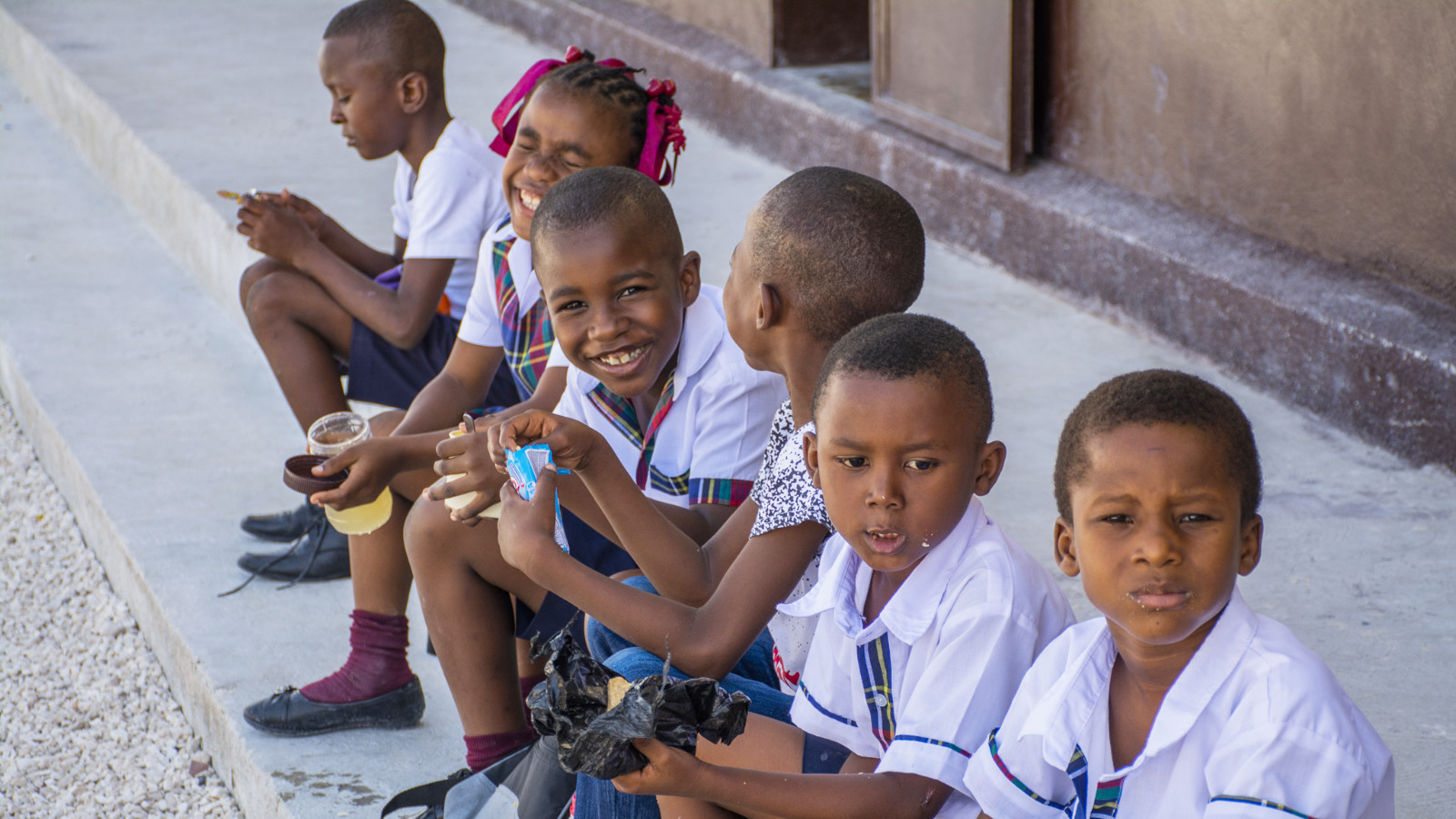 Haitian children in school uniforms eating snacks on curbside