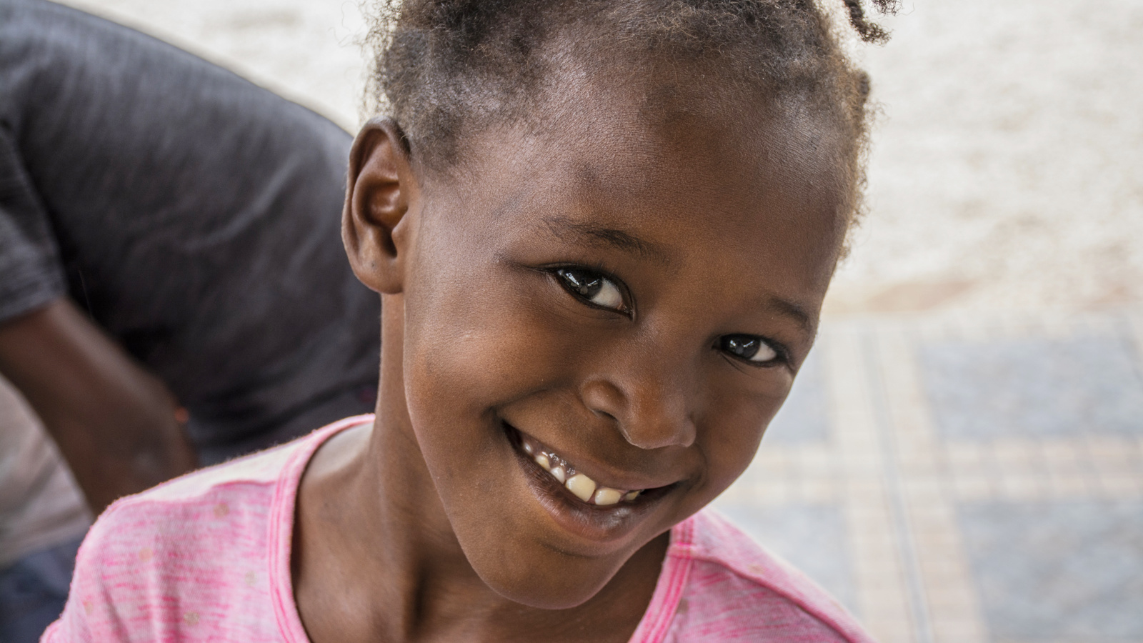 Young Haitian girl in a pink shirt smiling.