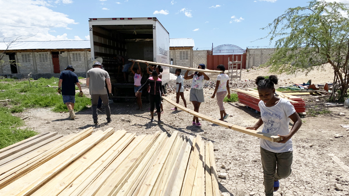 Volunteers and children unloading wooden boards from a trailer