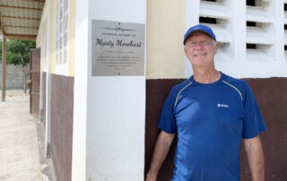 Greg Brashaw standing next to Marty Morehart memorial plaque on building in Haiti.