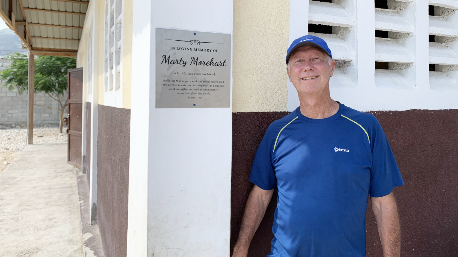 Greg Brashaw standing next to Marty Morehart memorial plaque on building in Haiti.