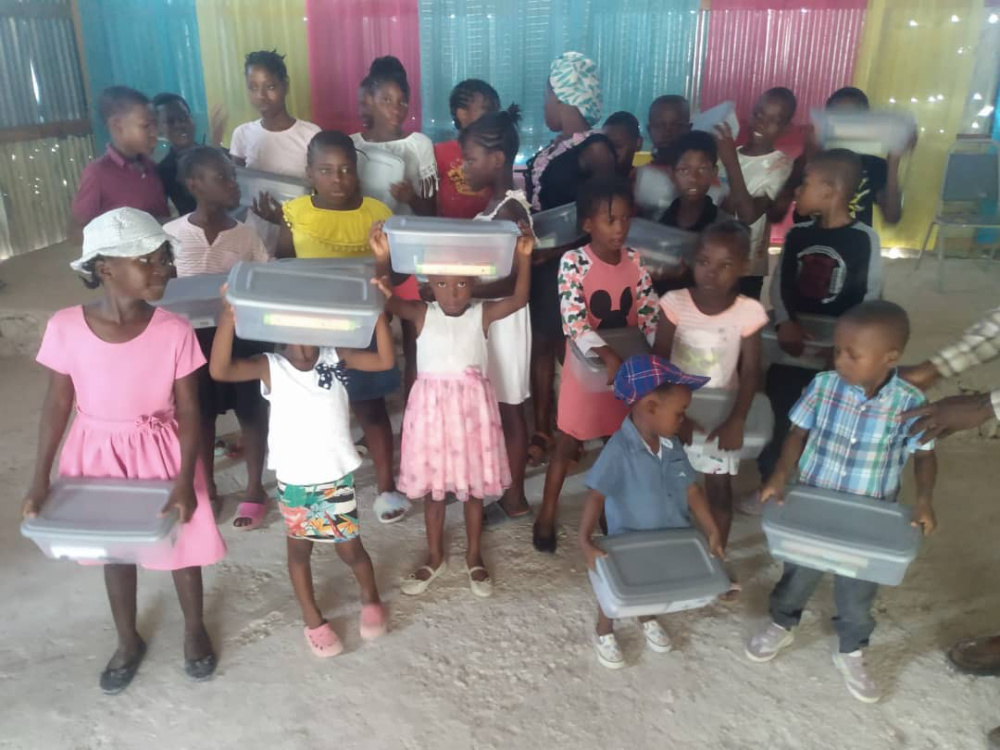 Haitian children holding their school books and supplies in clear bins