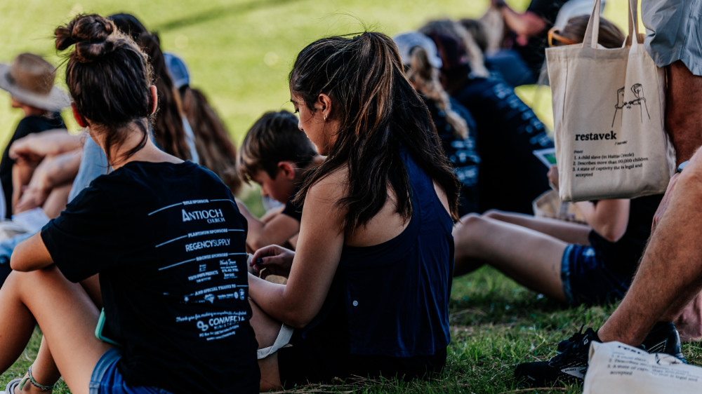 Group of sponsors and volunteers sitting on park lawn.