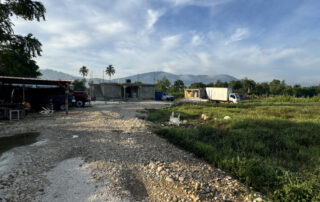 A gravel road leading to 3 small make shift buildings in Haiti country side.