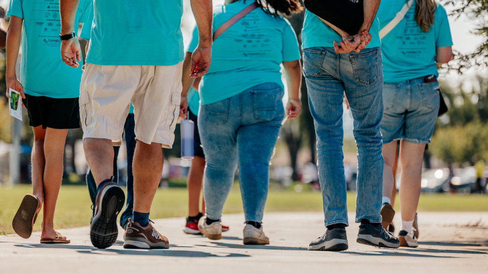 A group of people walking on a concrete path wearing matching blue restaveks walk 2024 t-shirts.