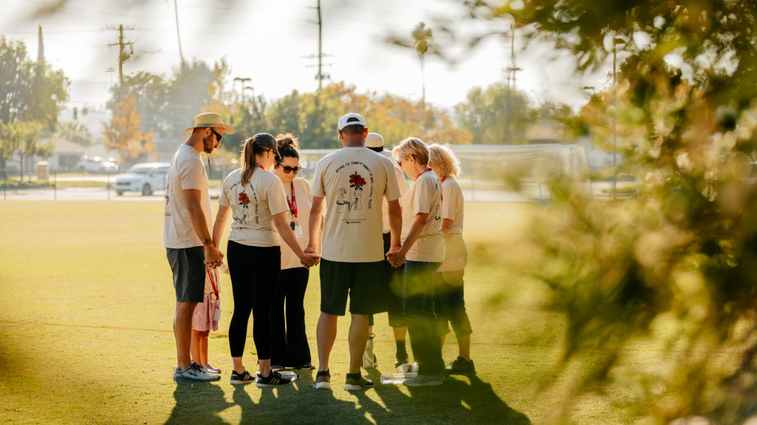 People in a park, joining hands in a circle, praying.