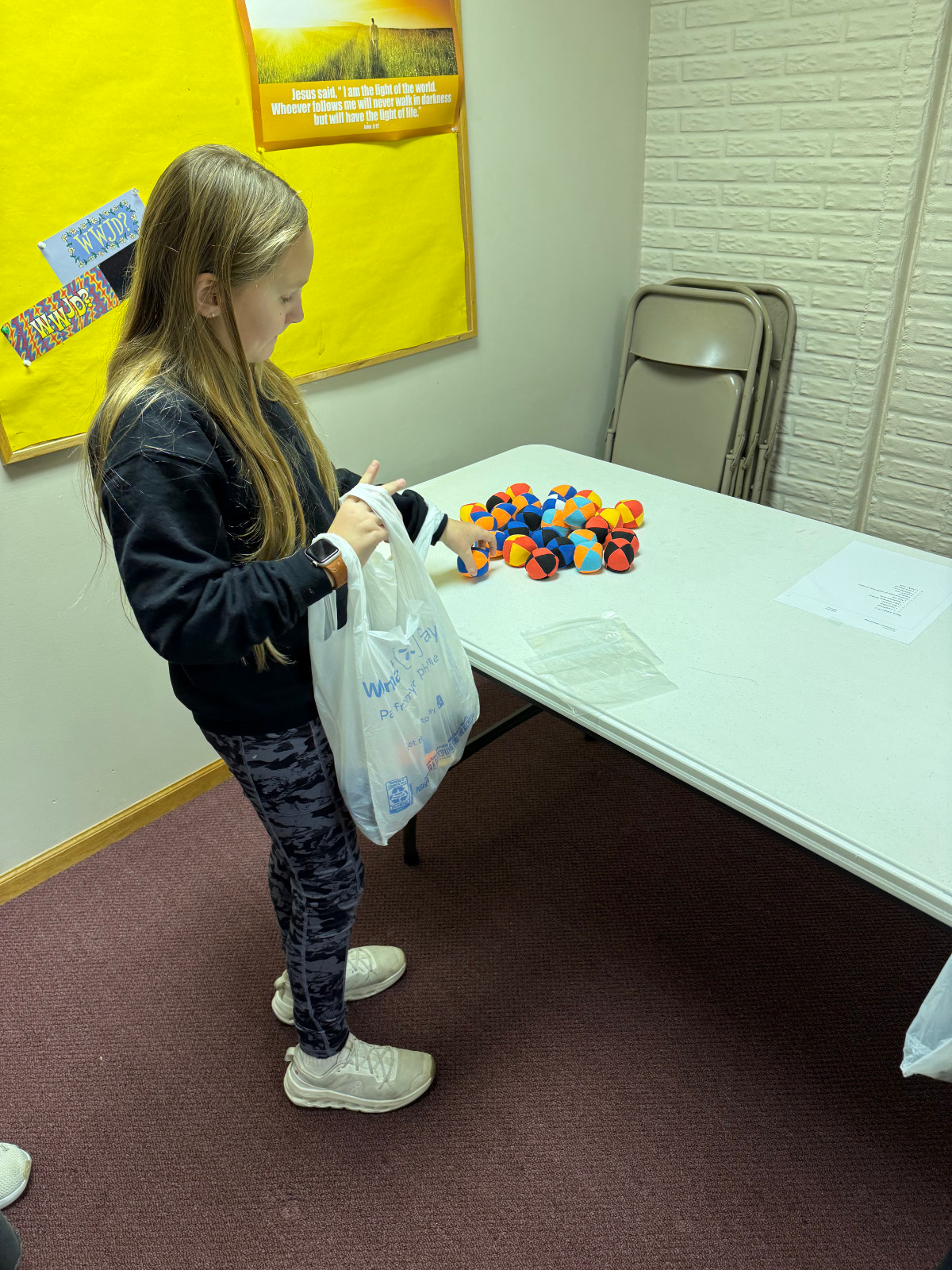AWANA volunteers, a female child at a table collecting toys for Christmas shoe box drive.