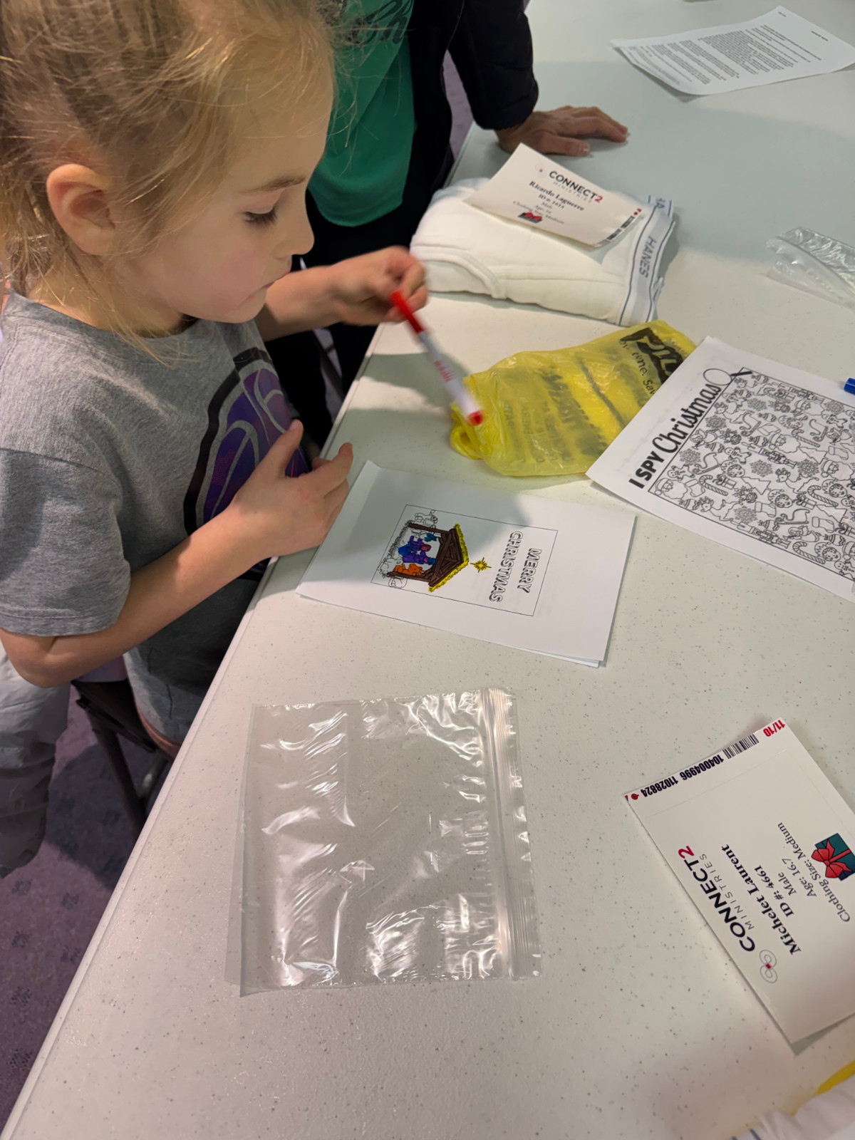 AWANA volunteers, a young female child at a table coloring cards for Christmas shoe box drive.
