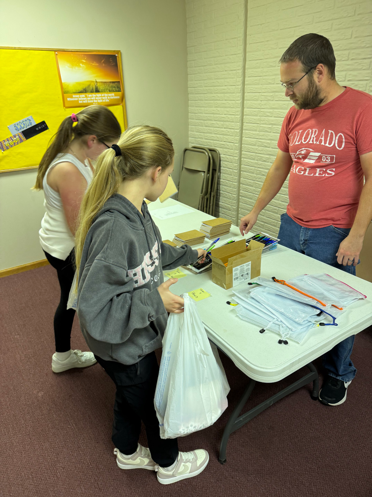 AWANA volunteers, adults and children at a table making collecting items for Christmas shoe box drive.