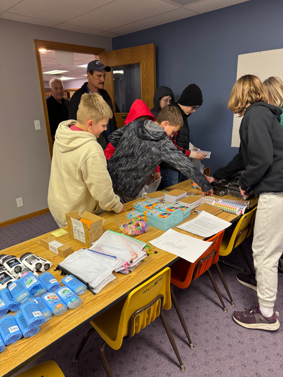 AWANA volunteers, adults and children lined up at a table collecting items for Christmas shoe box drive.